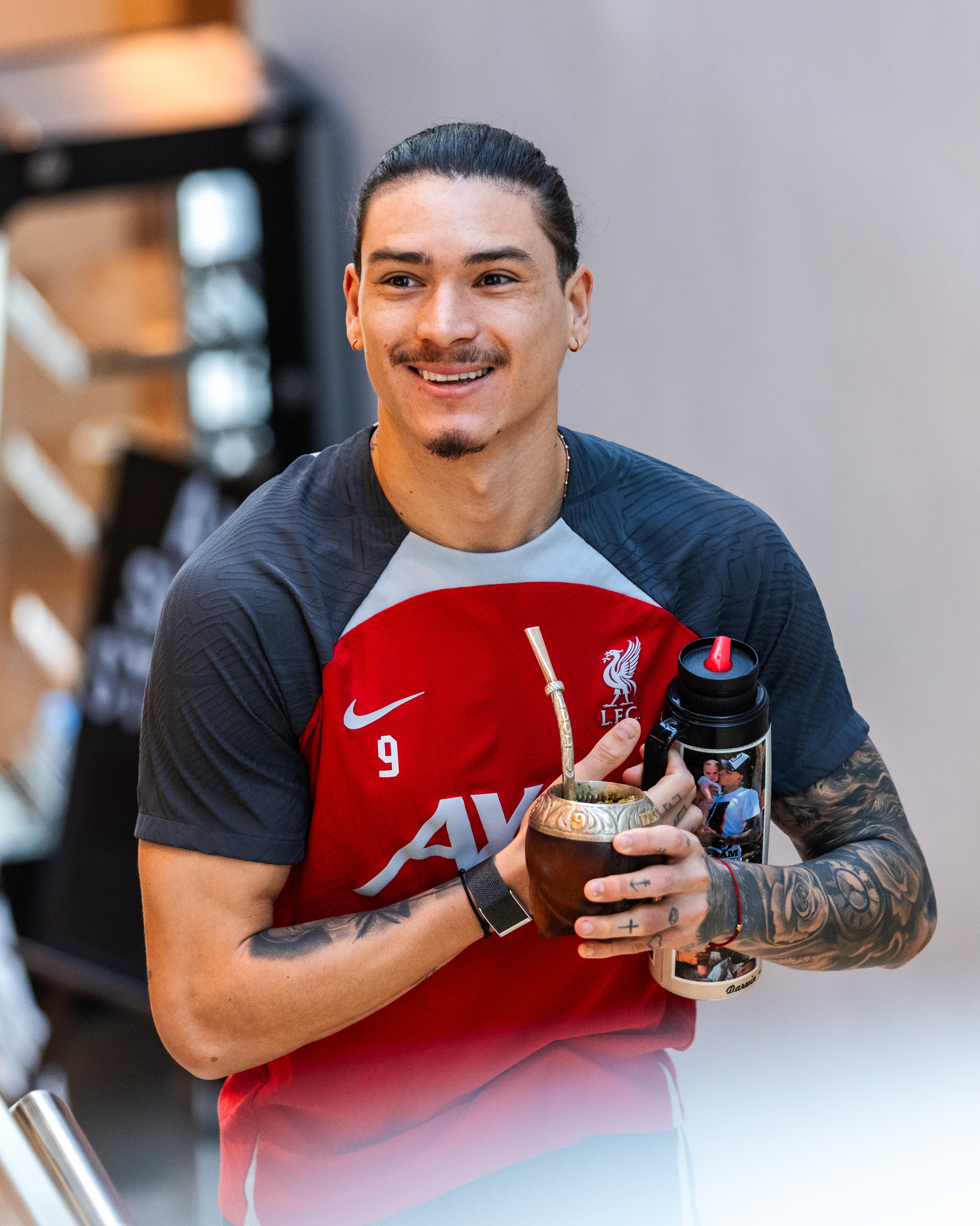 Darwin Nunez smiling while walking up the stairs at the AXA Training Centre holding a mate tea cup and flask.