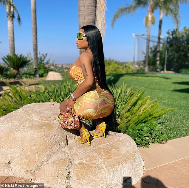 She rocks! The rapper, 38, worked a curve-clinging yellow dress, matching mesh heels and a huge pair of shades as she crouched on a massive boulder in a backyard